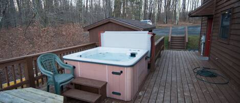 Une terrasse en bois avec un jacuzzi, un banc et une chaise.
