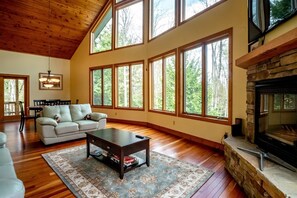 A spacious living room with a high ceiling, large windows, a fireplace, and a cozy seating area. - Bear Haven (Davis)