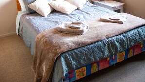 Un lit bien fait, avec une couette bleue et blanche, une tête de lit en bois et une table de chevet surmontée d’une lampe.