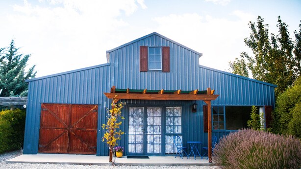 Un bâtiment de couleur bleue, de style grange, doté d’une grande porte en bois, d’un porche couvert et d’une partie avant avec des fenêtres.
