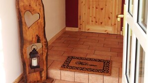 Una puerta de madera con un recorte en forma de corazón, un farol sobre un atril de madera y un felpudo en la entrada.