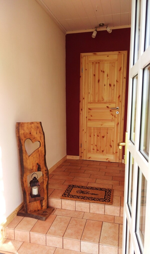A wooden door with a heart-shaped cutout, a lantern on a wooden stand, and a welcome mat at the entrance. - Apartment Marschperle (Neuendorf-Sachsenbande)