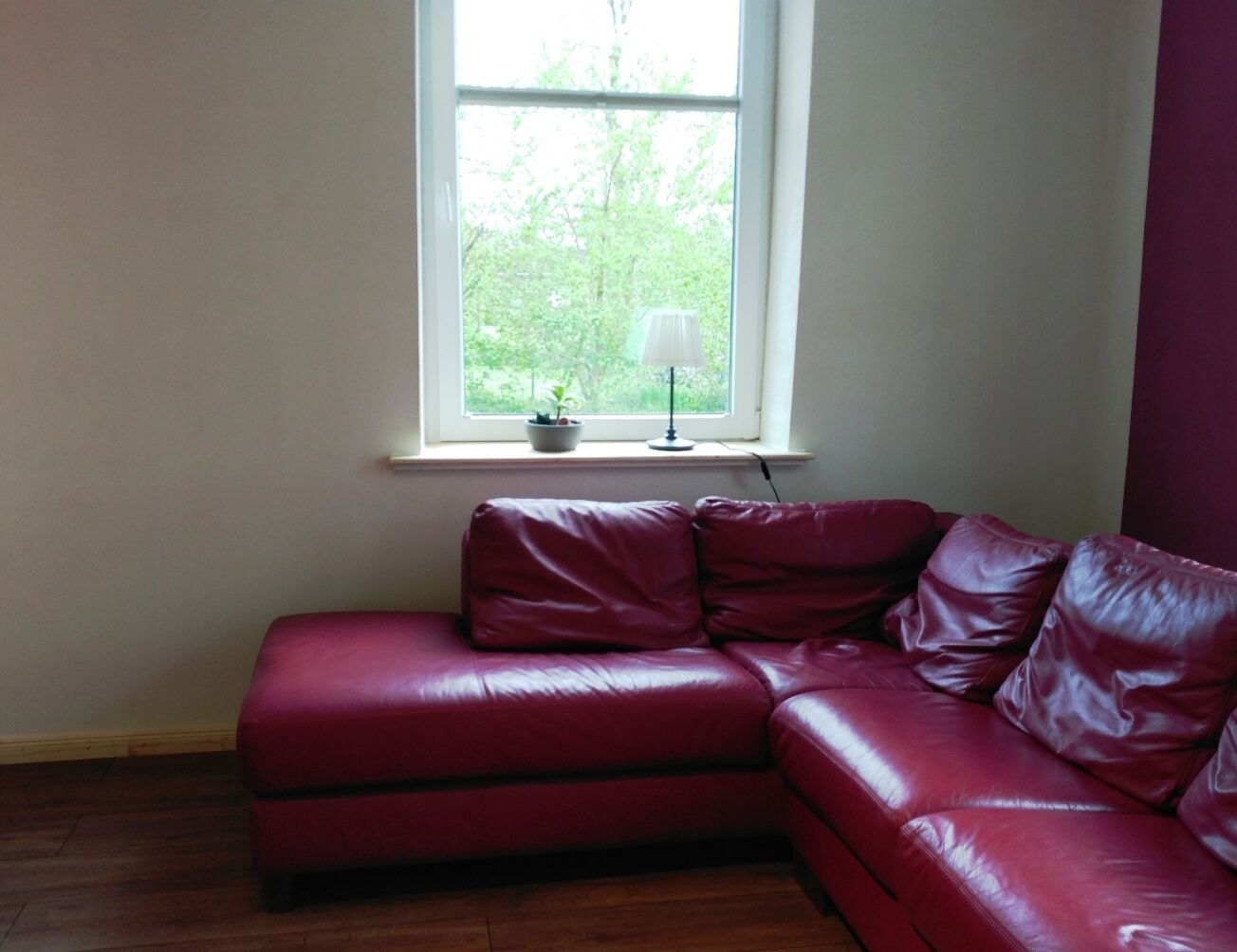 A red leather sectional sofa in a room with a window, a small table with a lamp, and a potted plant.