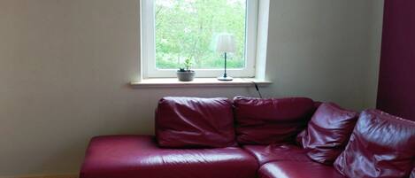 A red leather sectional sofa in a room with a window, a small table with a lamp, and a potted plant.