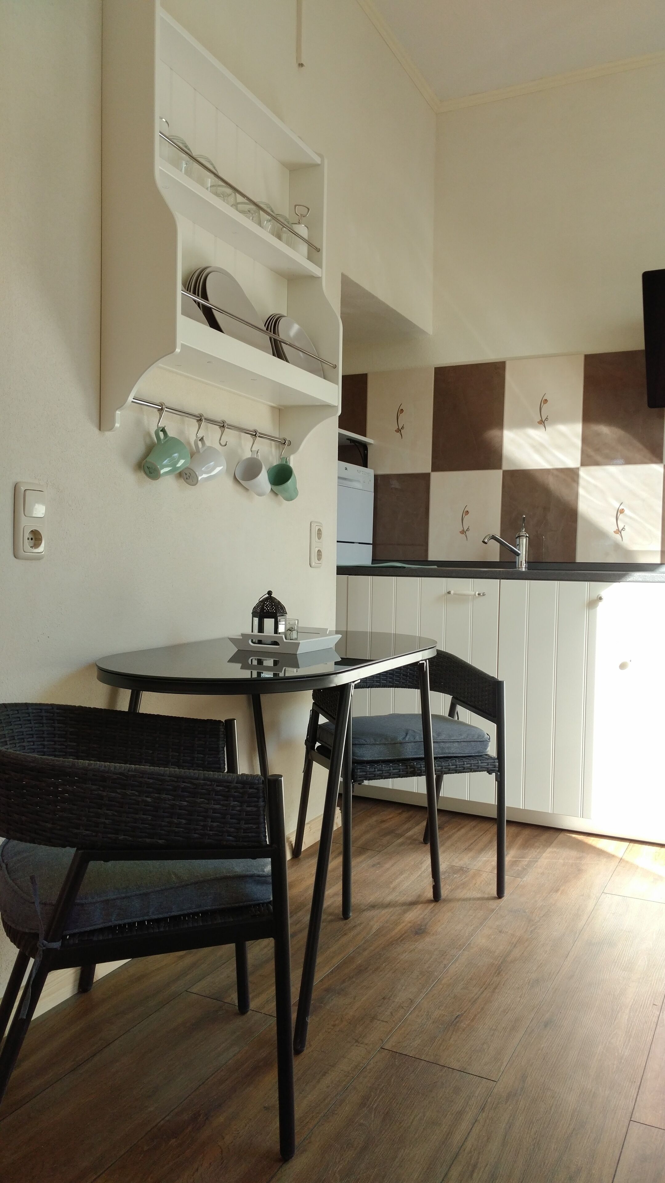 A small kitchen with a dining table and chairs, a built-in shelf with dishes, and a checkered backsplash.