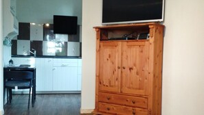 Una habitación con un armario de madera, un televisor encima y un sofá rojo, con una cocina al fondo.