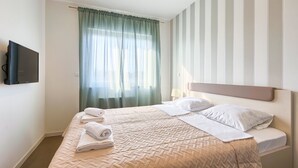 Ein ordentlich bezogenes Bett mit einer beigen Steudecke, einem grünen Vorhang und einer gestreiften Wand.
