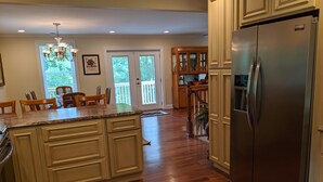 A kitchen with wooden flooring, a large island, a refrigerator, and a dining area with chairs and a table.