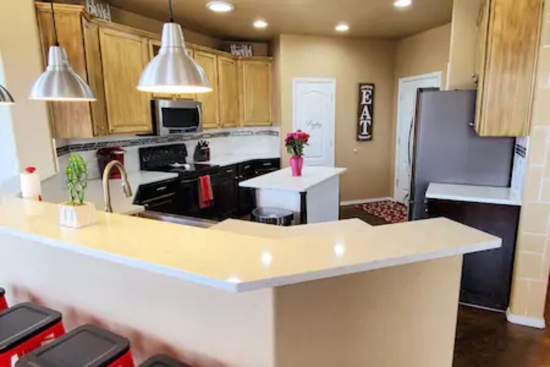A modern kitchen with wooden cabinets, a central island, pendant lighting, and a refrigerator.