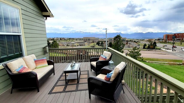 Um terraço com móveis de vime e vista para a paisagem urbana e montanhas.