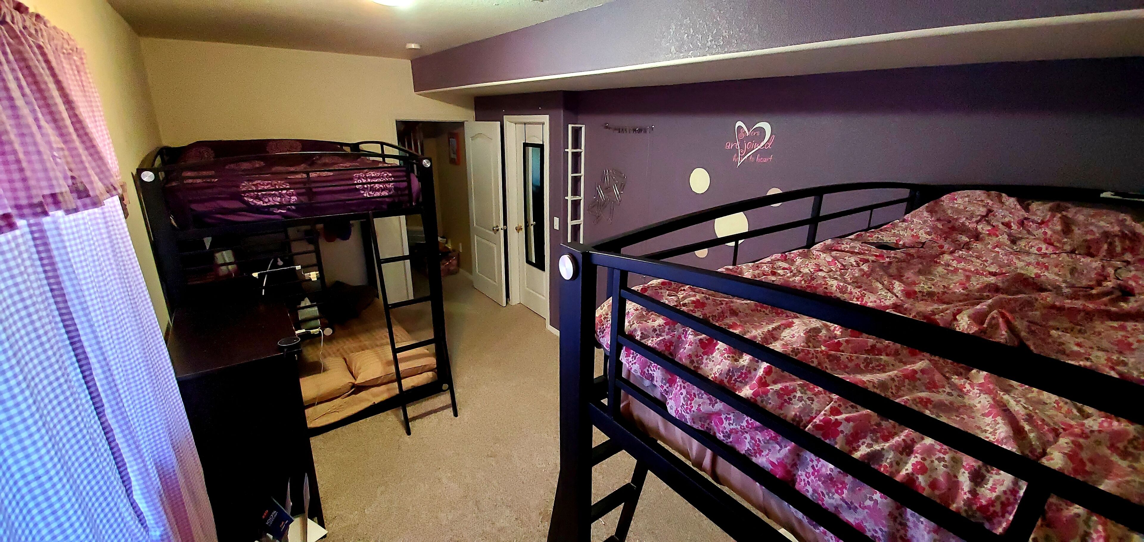 A dormitory room with bunk beds, a desk, and a door leading to another room.