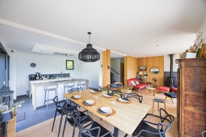 Una cocina moderna con una isla central, comedor con sillas, una mesa de madera y un espacio de sala de estar acogedor con chimenea.