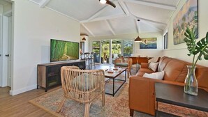 A spacious living area with a large TV, wicker chairs, a coffee table, and a ceiling fan.