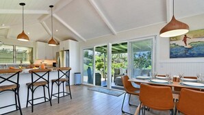 A modern kitchen with a large island, bar stools, and a dining area with orange chairs.