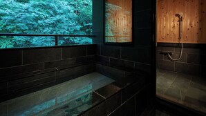 Un baño moderno con una bañera grande, zona de ducha y pared de madera que proyecta un paisaje de bosque.
