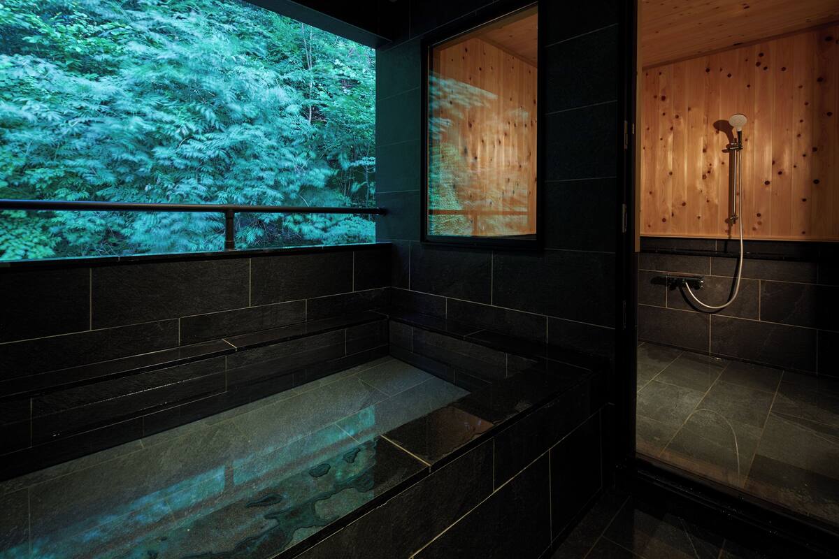 Un bagno moderno con una grande vasca da bagno, una zona doccia e un pannello di legno con proiezione di una scena forestale.