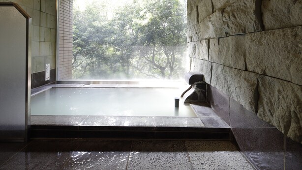 Baño de aguas termales con vistas a árboles, paredes de piedra y suelo de baldosas.