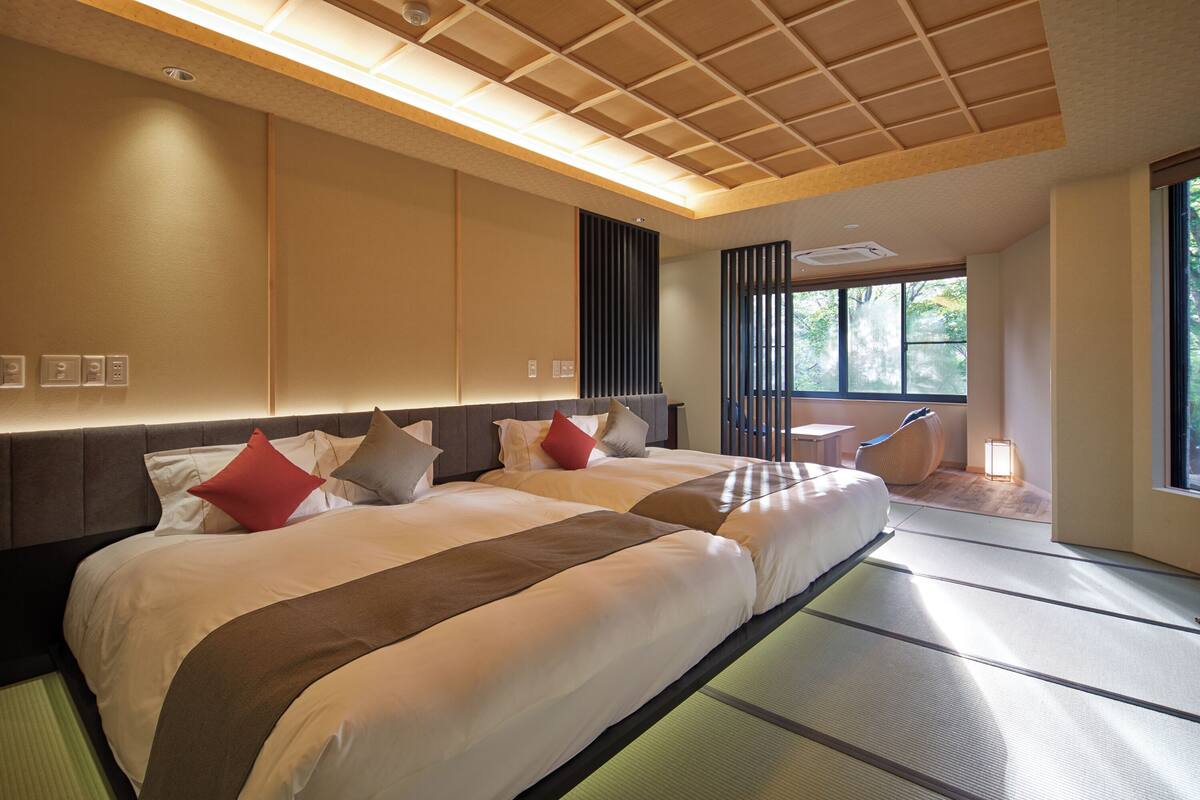 Una camera d'albergo con due letti, una grande finestra e un pavimento in tatami tradizionale.
