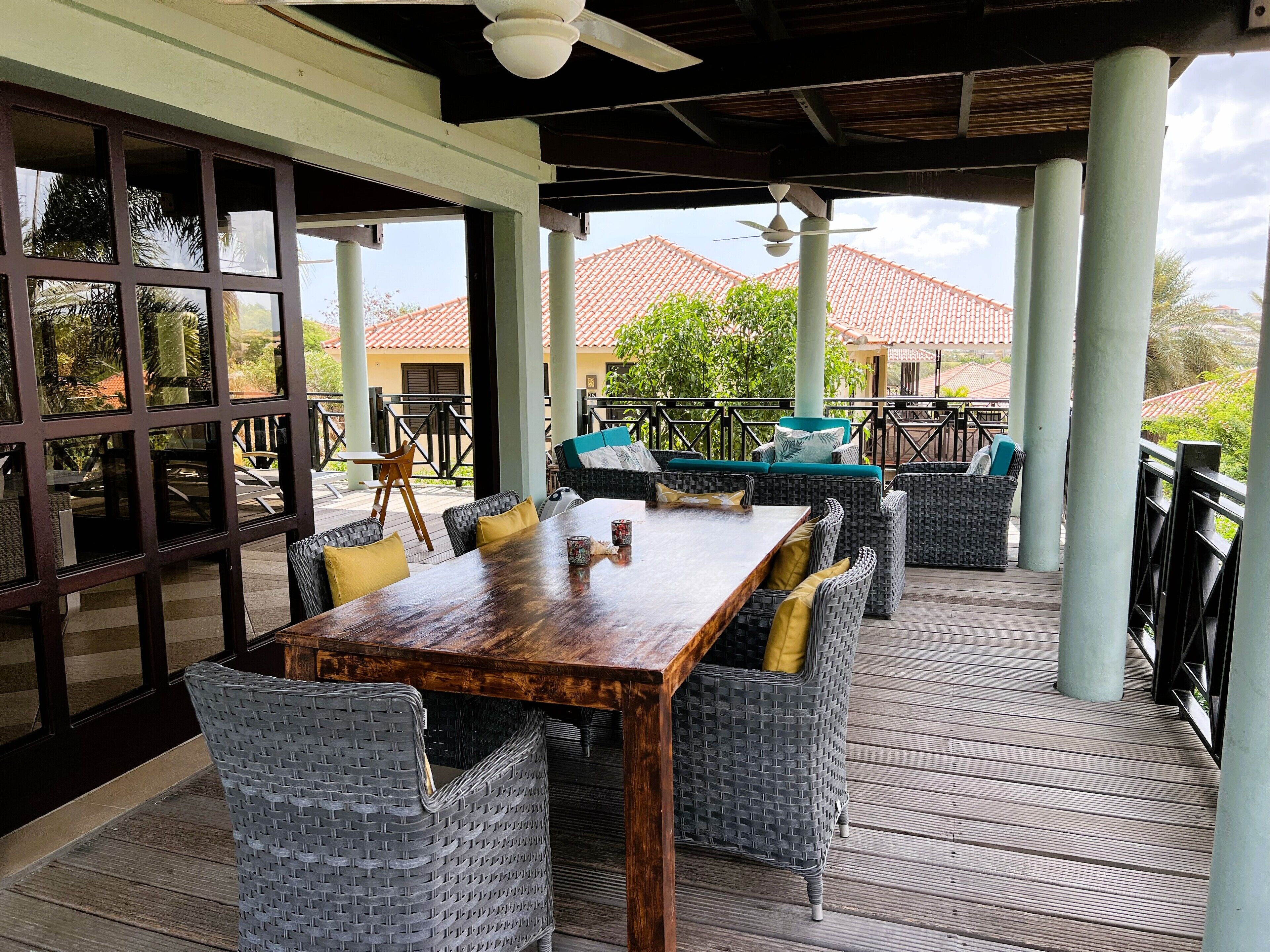 Un espace extérieur aménagé en terrasse, avec une table en bois et des chaises en osier, entouré d’une balustrade et de colonnes.