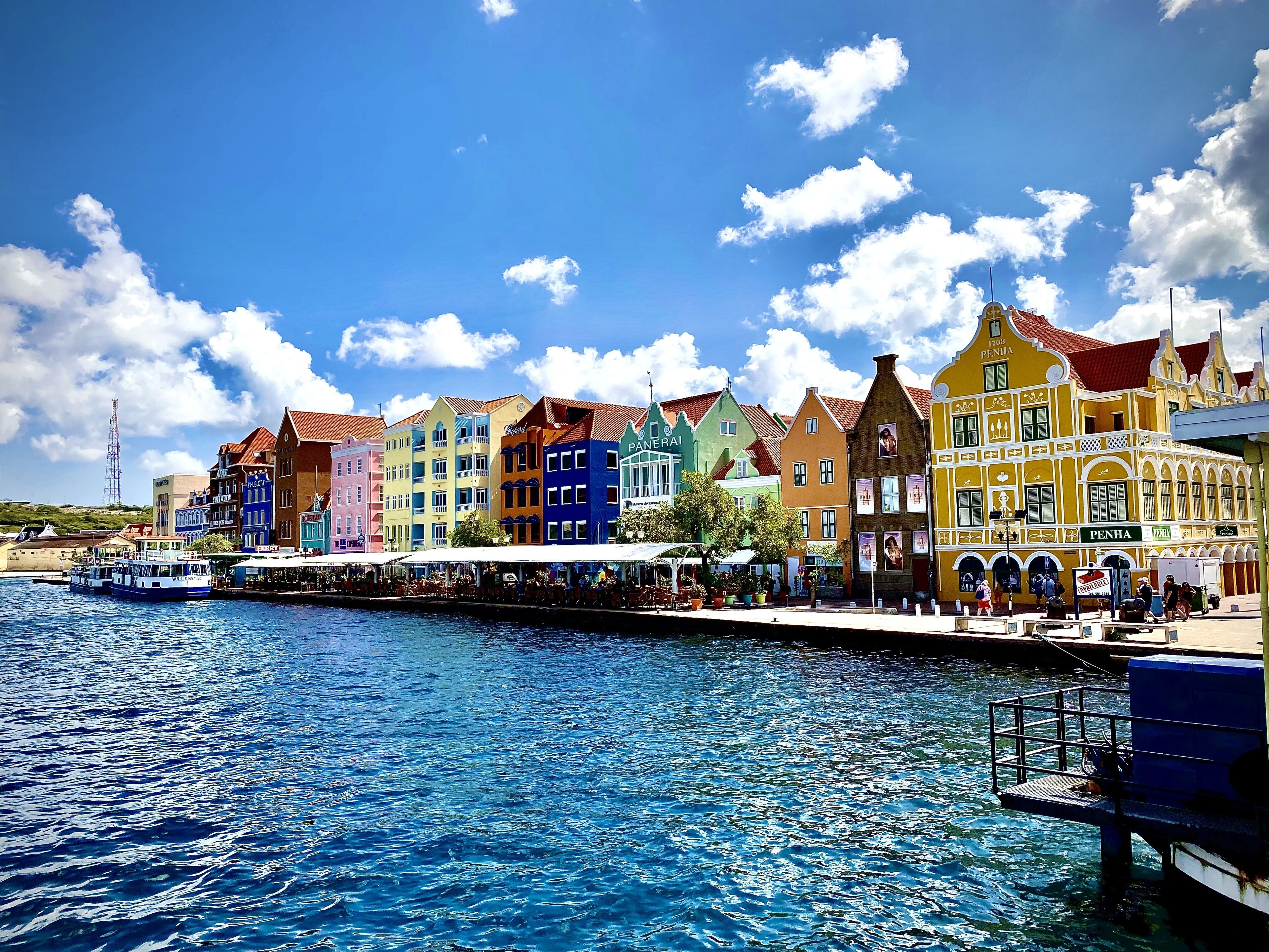 A waterfront with colorful buildings, a dock with boats, and a clear blue sky.