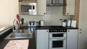 A compact kitchen with a microwave, toaster, stove, oven, and sink. - Cairngorms Flower Lodge (Aviemore)