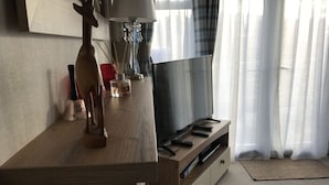 A wooden TV stand with a flat-screen TV, remote controls, and a decorative wooden animal figure. - Cairngorms Flower Lodge (Aviemore)