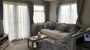 A cozy living room with a sofa, a coffee table, and a TV. - Cairngorms Flower Lodge (Aviemore)