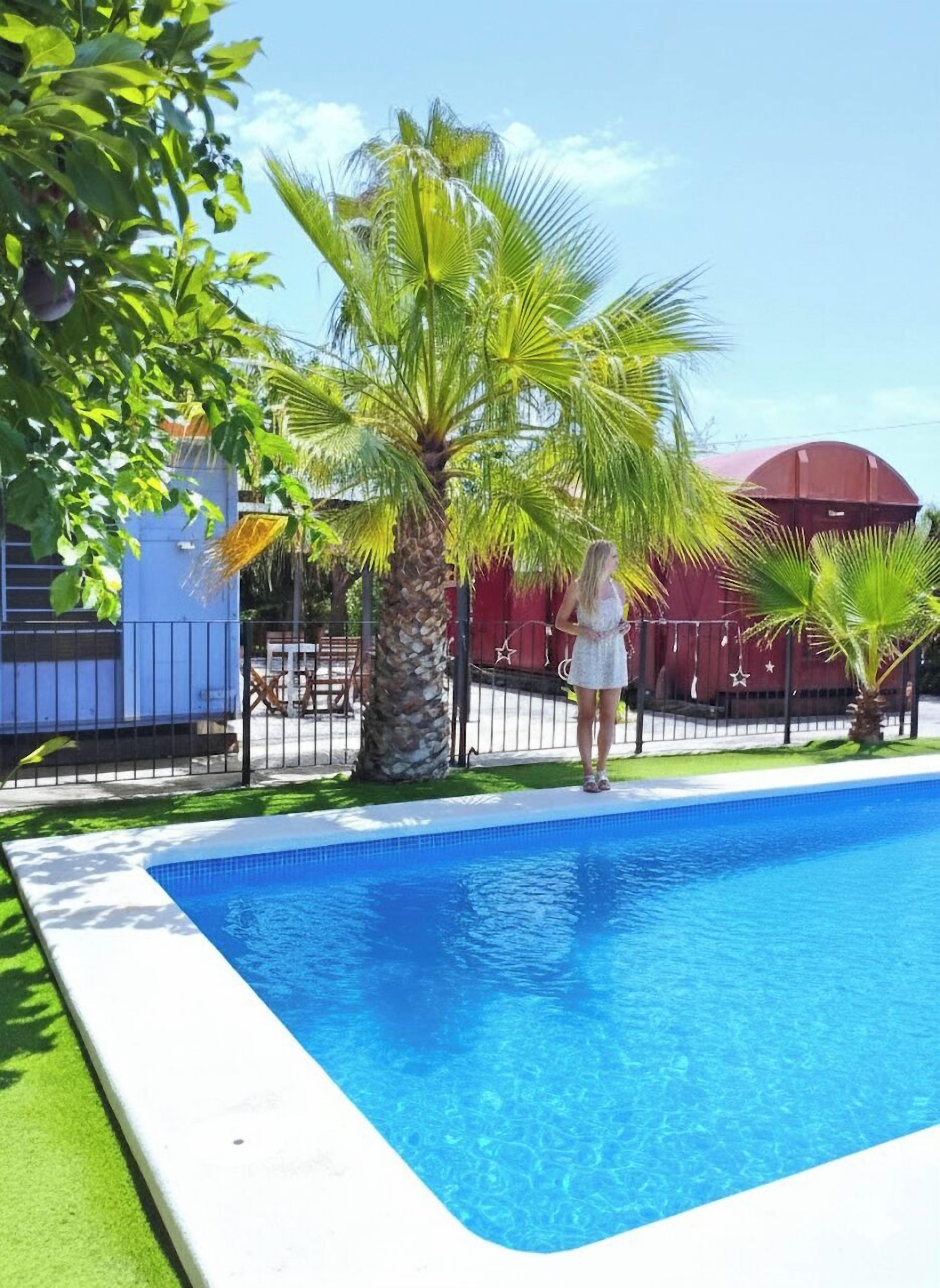 A swimming pool with a clear blue water surface, surrounded by a white pool deck and green artificial grass.