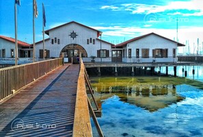 Un muelle de madera que conduce a un edificio blanco con techo rojo, un emblema de estrella y un cartel que dice "Club Nautico Mar Menor".