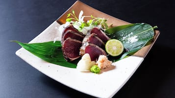 Une assiette carrée contenant de la viande en tranches, du citron vert et diverses garnitures, le tout présenté sur un fond sombre.