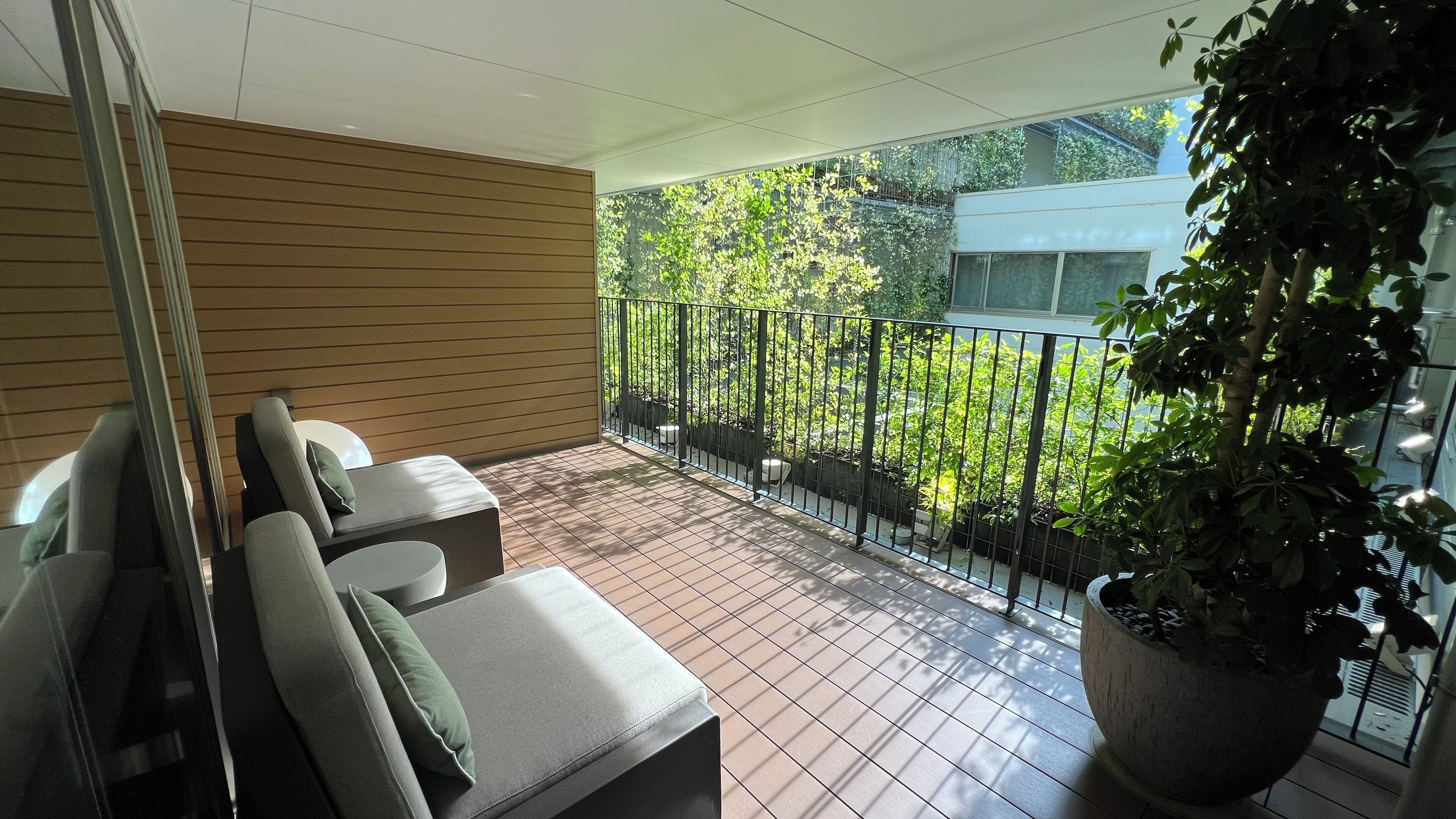A balcony with a seating area, a potted plant, and a view of greenery and a building.