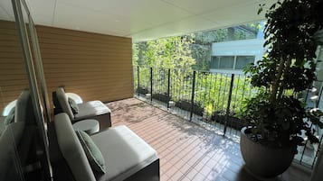 A balcony with a seating area, a potted plant, and a view of greenery and a building.