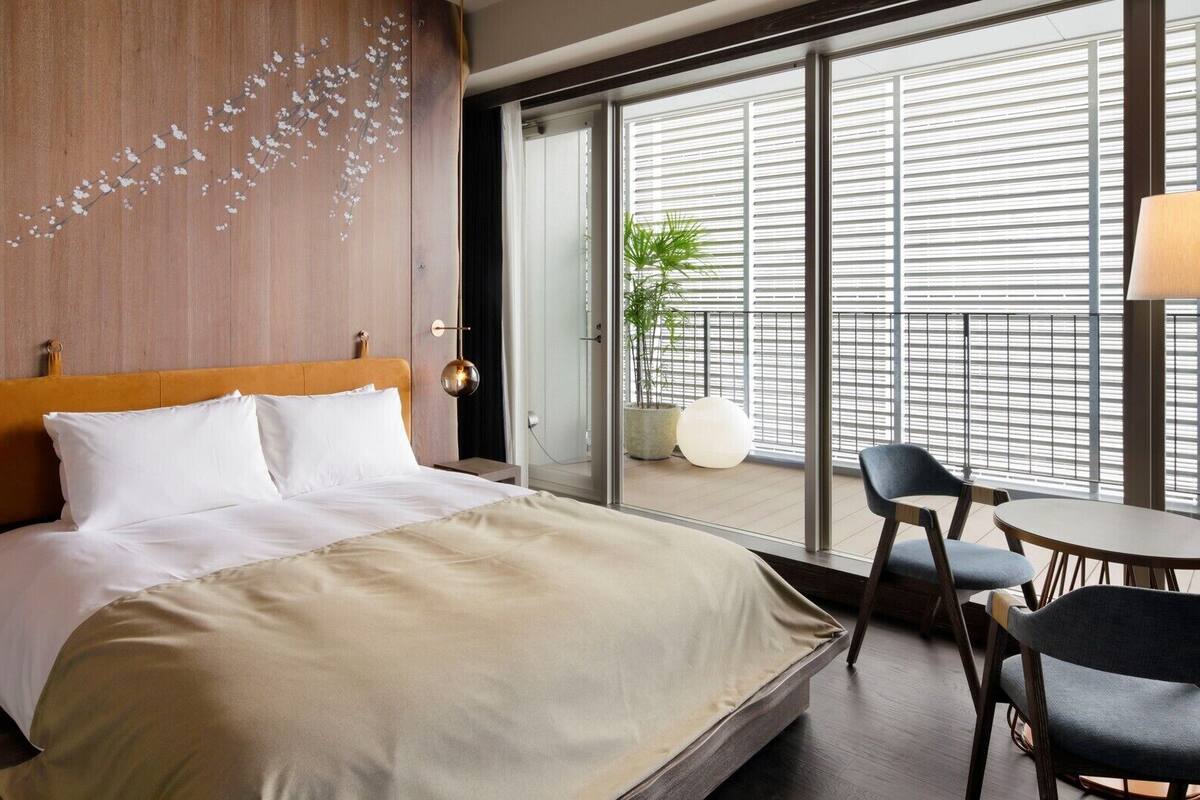 Ein Hotelzimmer mit einem großen Bett, einem Holzkopfteil, einer Schiebeglasdoor zum Balkon, einem runden Tisch und zwei Stühlen.
