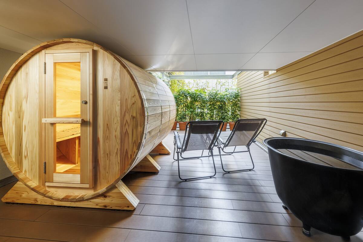 Ein Sauna-Raum mit einem hölzernen Saunafass, zwei Stühlen und einer schwarzen Badewanne.
