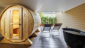 Une salle de sauna comprenant un tonneau de sauna en bois, deux chaises et une baignoire noire.