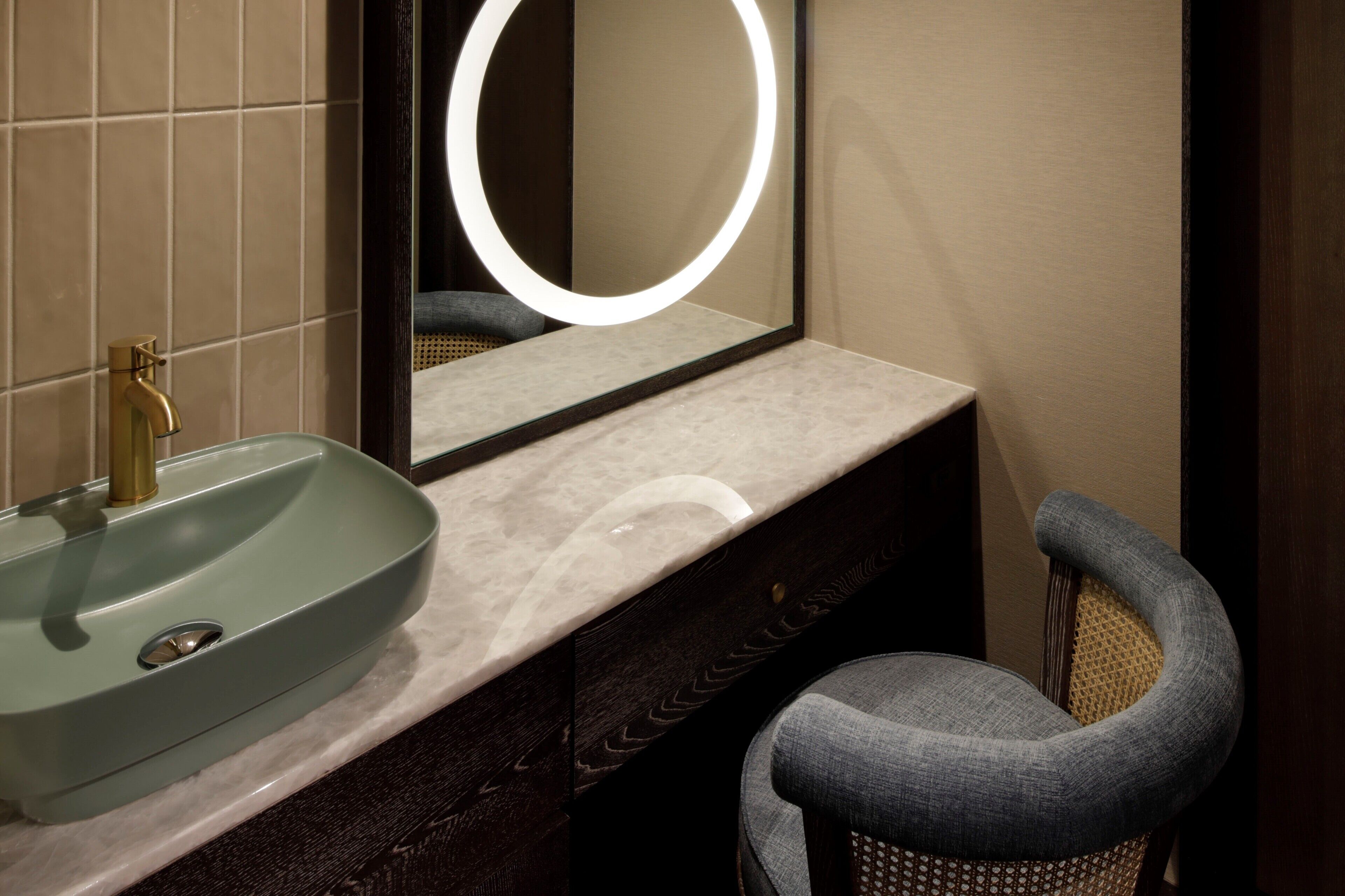 A bathroom with a sink, mirror, and chair.