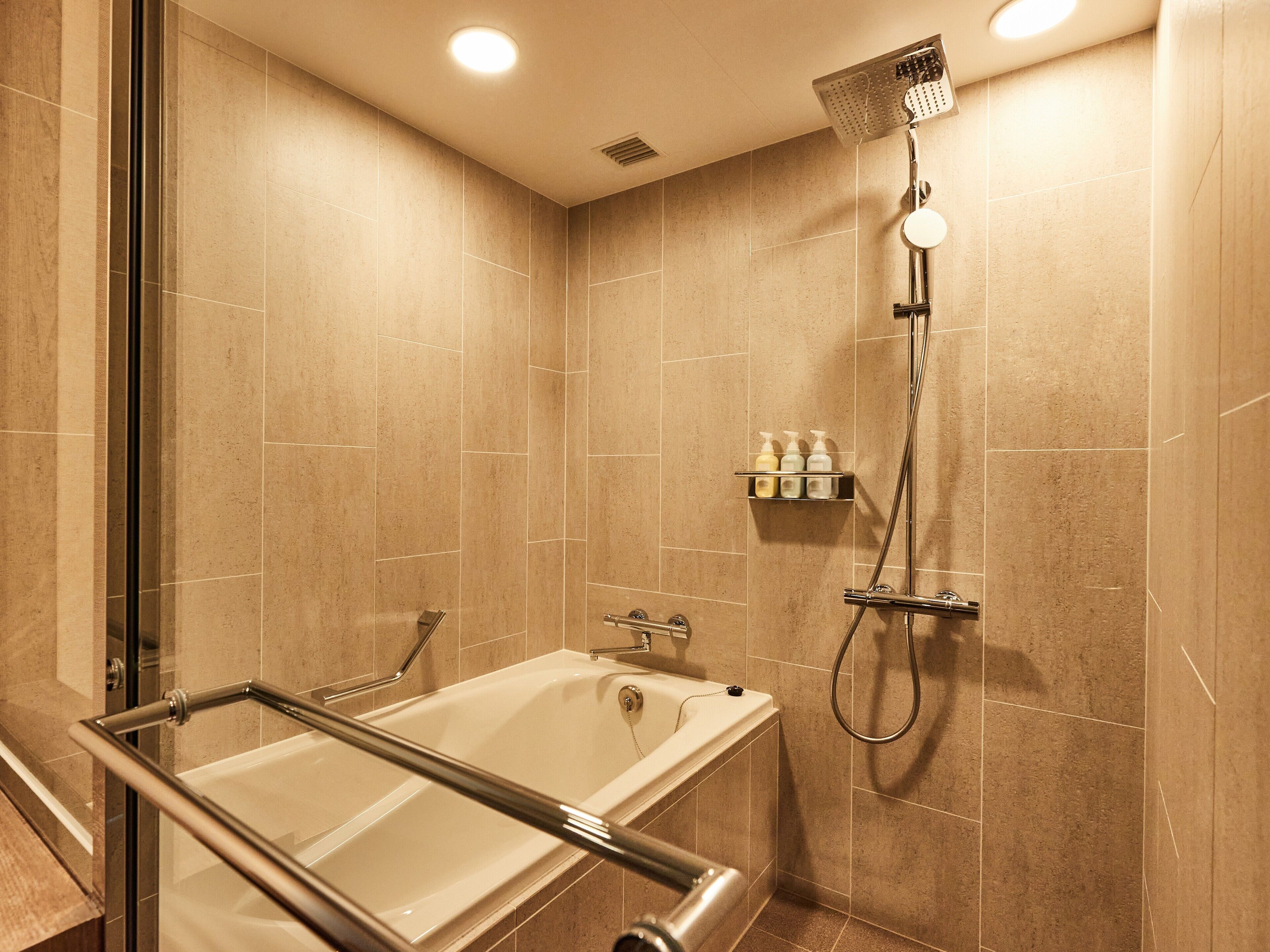 Ein modernes Badezimmer mit einer gläsernen Badewanne, einer Duschbrause und einem Ablagefach mit Pflegeprodukten.