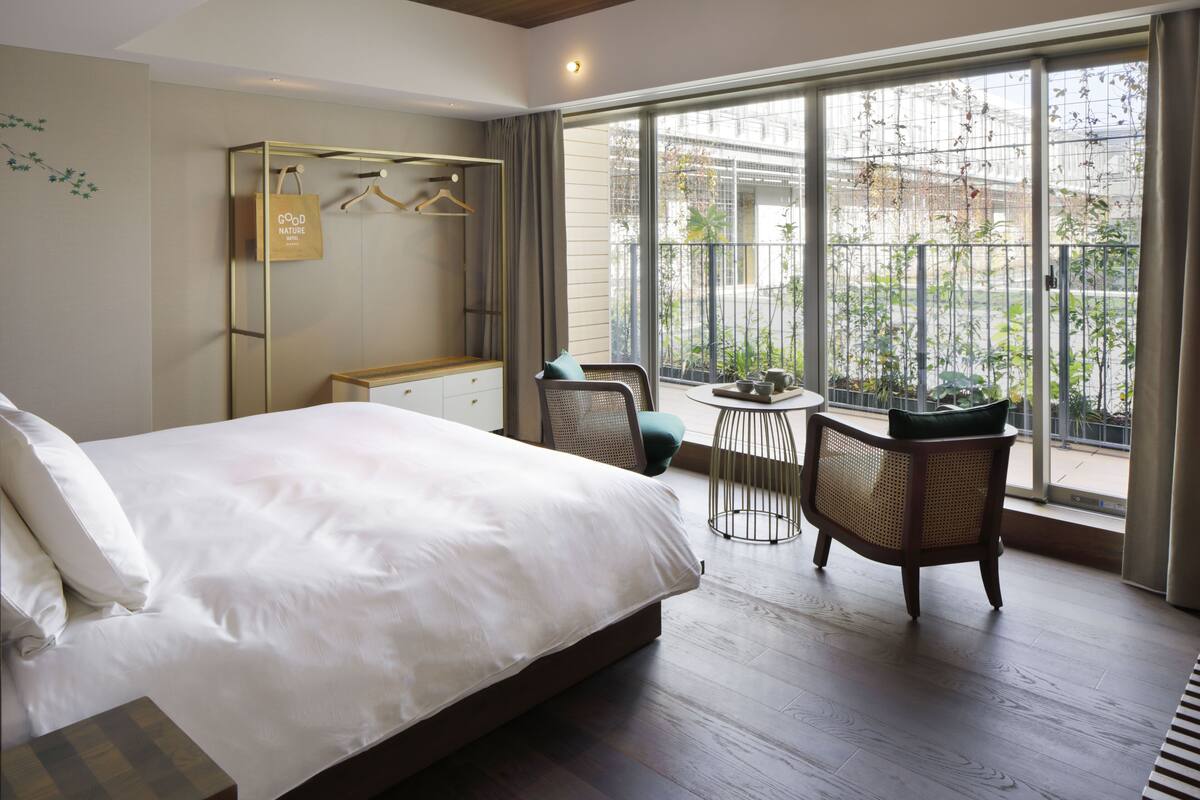 Ein Schlafzimmer mit einem großen Bett, einem Kleiderschrank, einer Sitzecke mit Tisch und einem Balkon mit Pflanzen.