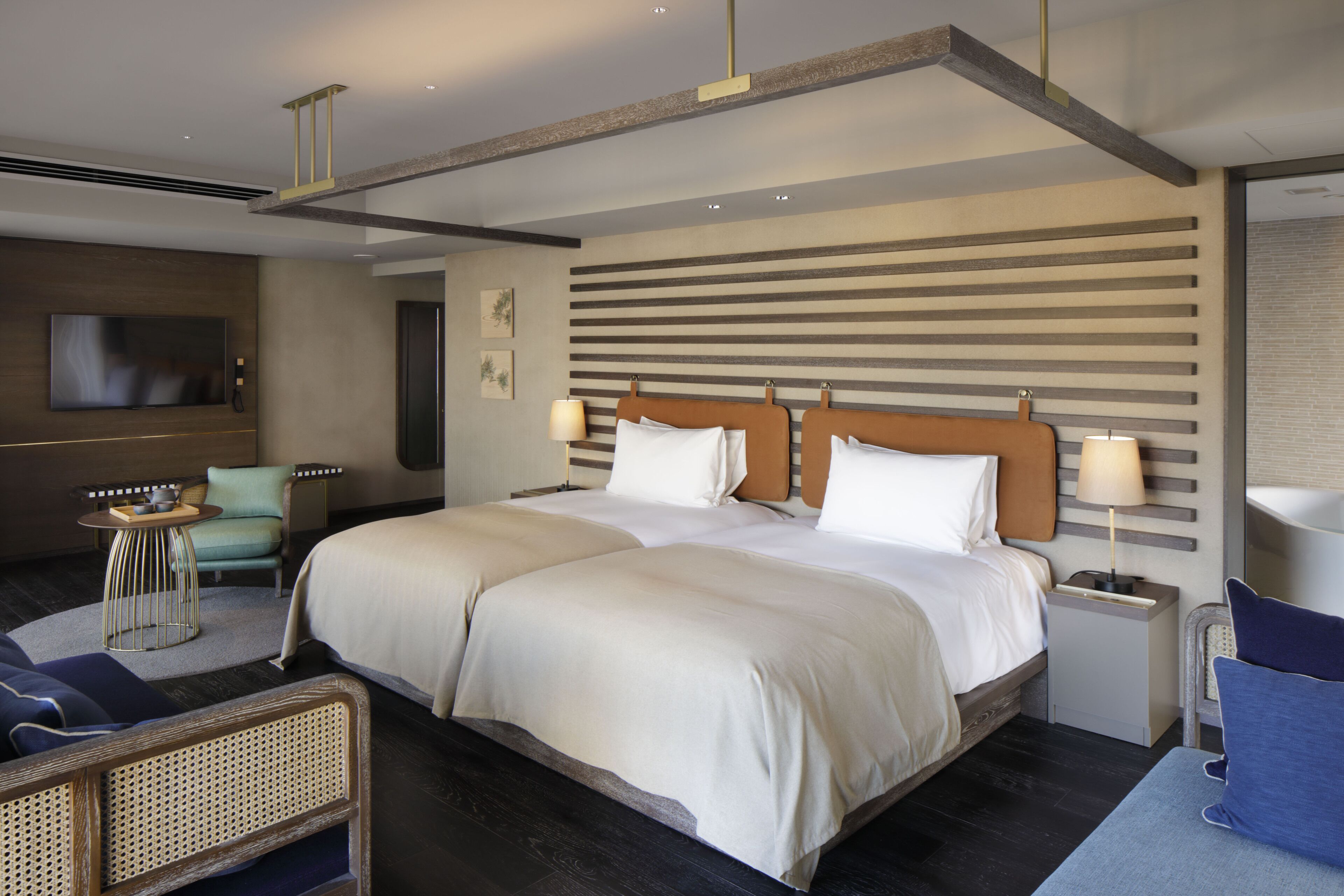 Una habitación de hotel moderna con una cama grande, un televisor de pantalla plana, un escritorio con lámpara y una zona de estar con una silla y una mesa pequeña.