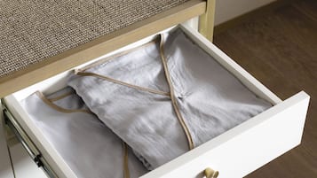 A white drawer with a brass handle, containing folded white linens tied with a beige string.