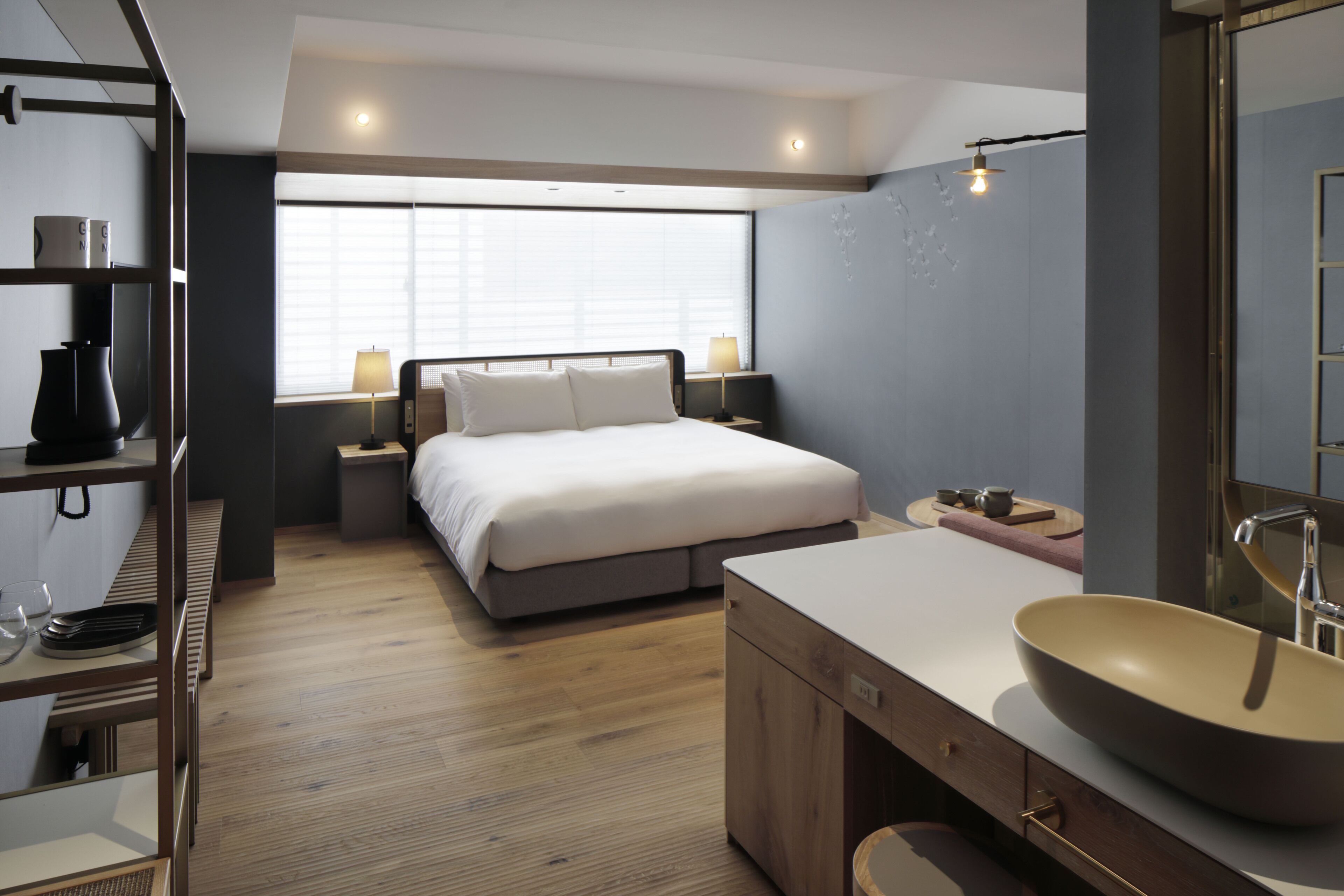 Un dormitorio moderno con una cama grande, mesitas de noche, piso de madera, un ventanal amplio y un baño con lavamanos y espejo grandes.