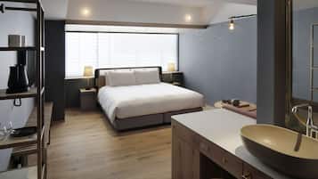 A modern bedroom with a large bed, bedside tables, a wooden floor, a large window, and a bathroom with a large sink and mirror.