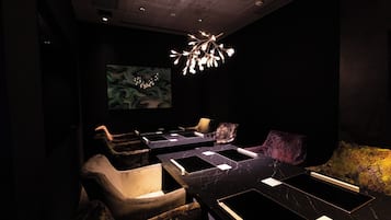 A dimly lit room with a modern chandelier, several leather chairs, and a large abstract painting on the wall.