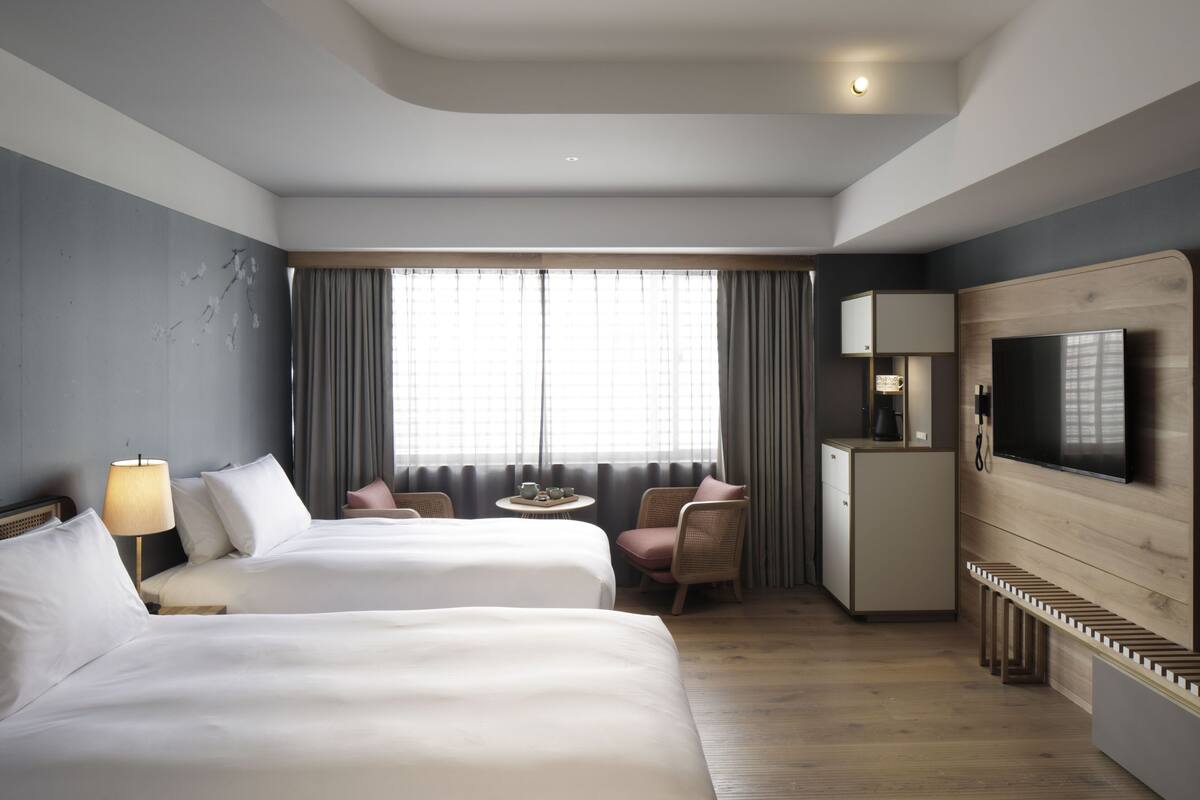 Ein Hotelzimmer mit zwei Betten, einem Schreibtisch, einem Fernseher und einer kleinen Küchenzeile.