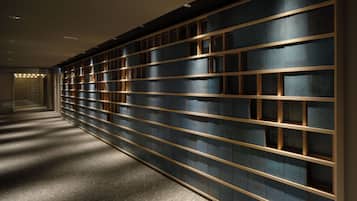 A hallway with a wall of dark blue panels and golden frames, leading to a well-lit area.