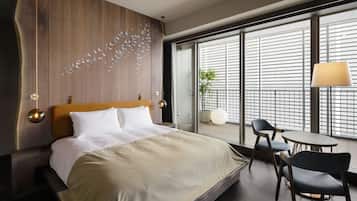 Une chambre d’hôtel moderne avec un grand lit, une tête de lit en bois, un balcon avec vue et une petite table avec des chaises.