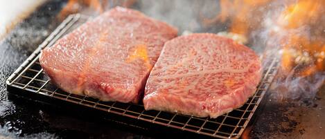 Two steaks cooking on a grill with visible flames and smoke.