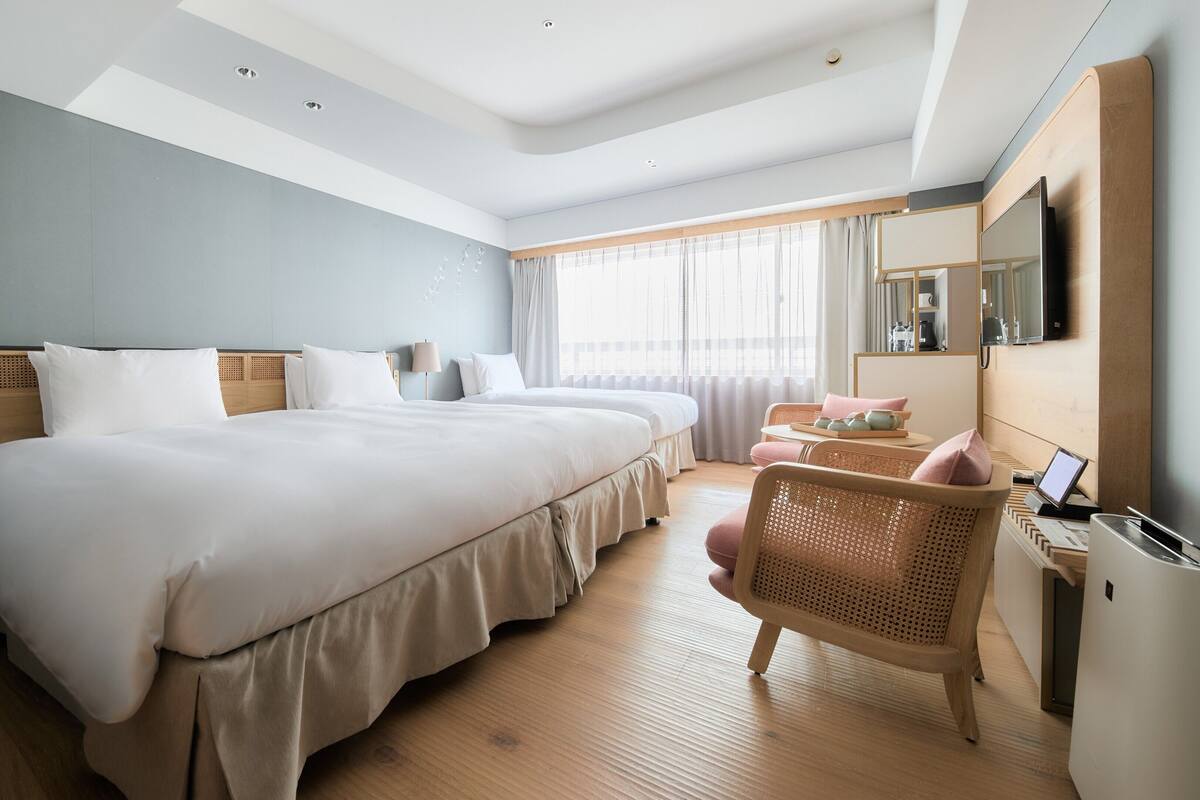 Ein Hotelzimmer mit einem großen Bett, Nachttischen, einem Schreibtisch mit Computer und einem Fenster mit Vorhängen.