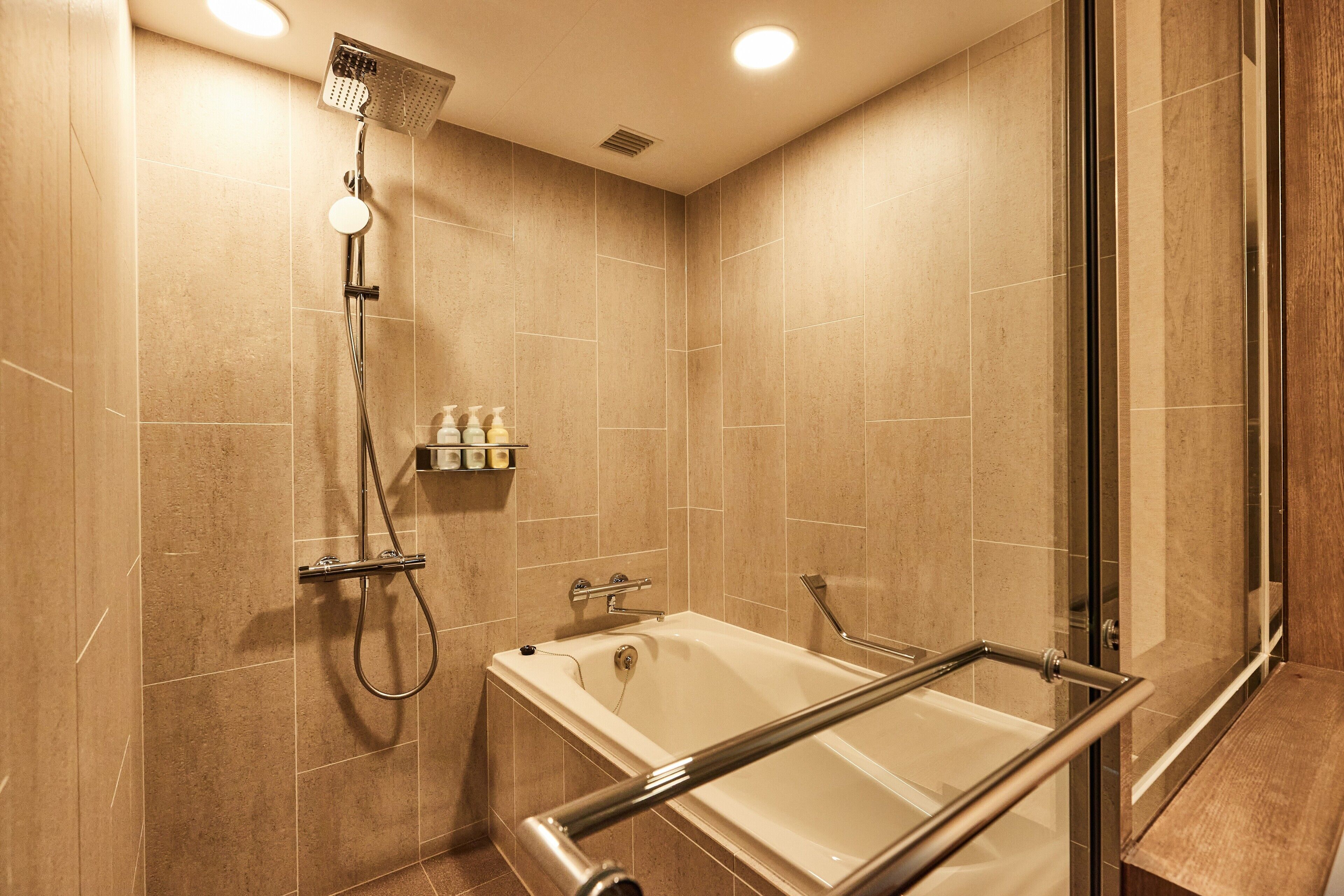 Un baño moderno con cabina de ducha de vidrio, bañera con mampara de vidrio y paredes con azulejos color beige.