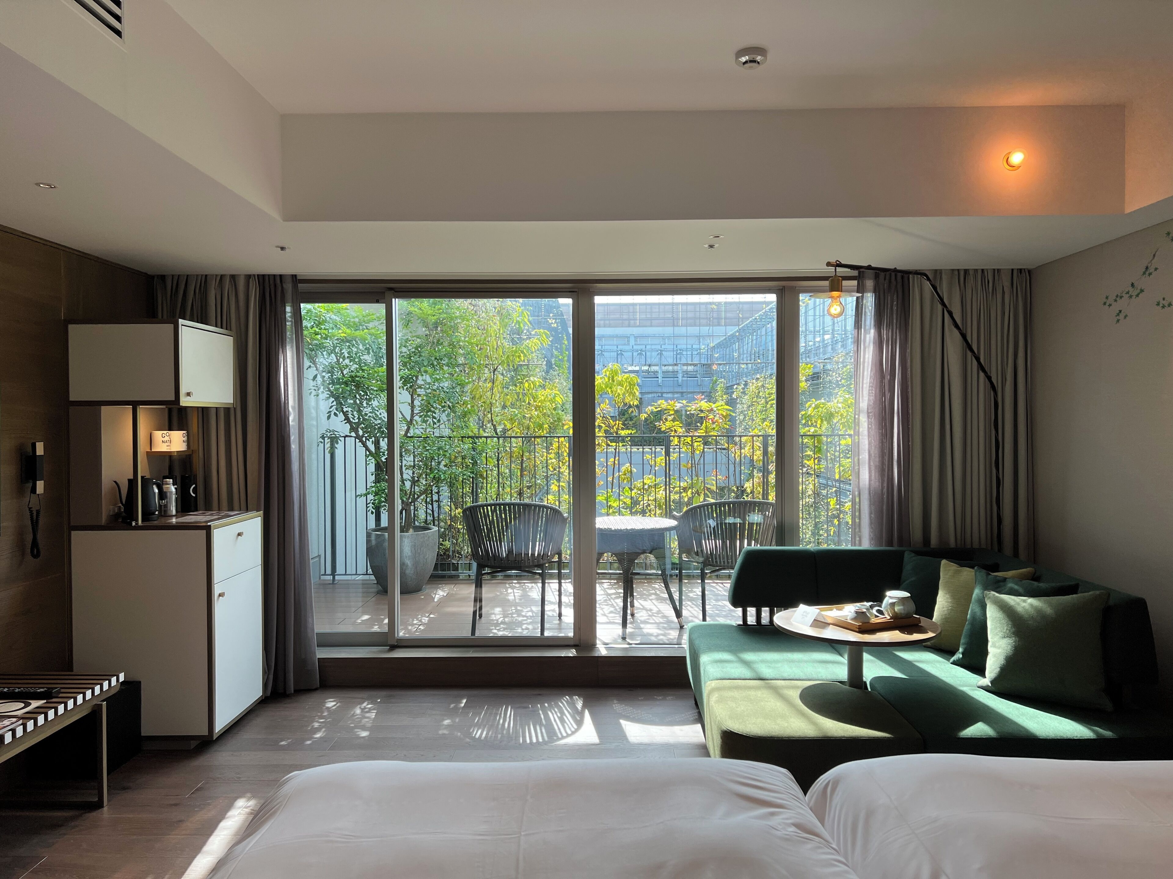 Habitación de hotel con cama, sofá, mesa de comedor, escritorio y vistas al balcón exterior.